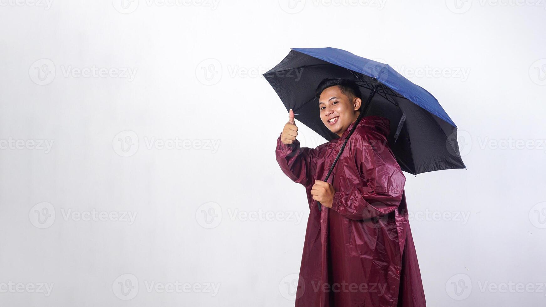 Happy Asian man in red raincoat holds umbrella and showing his thumb up isolated on white background photo