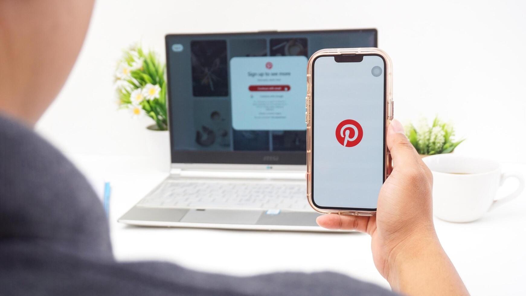 Yogyakarta, Indonesia, April 2025 - Man holding smartphone that shows front page of Pinterest, visual discovery platform application on the screen isolated on white background photo