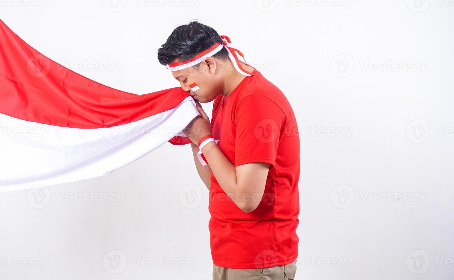 Indonesian man celebrate Indonesia independence day on August 17 by kissing the Indonesian flag solemnly isolated on white background photo