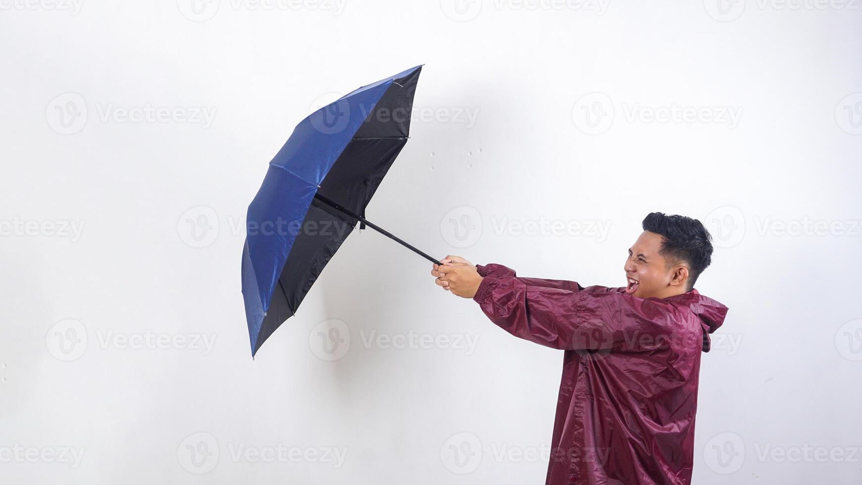 Asian man in red raincoat holds umbrella tightly because of the strong wind isolated on white background photo