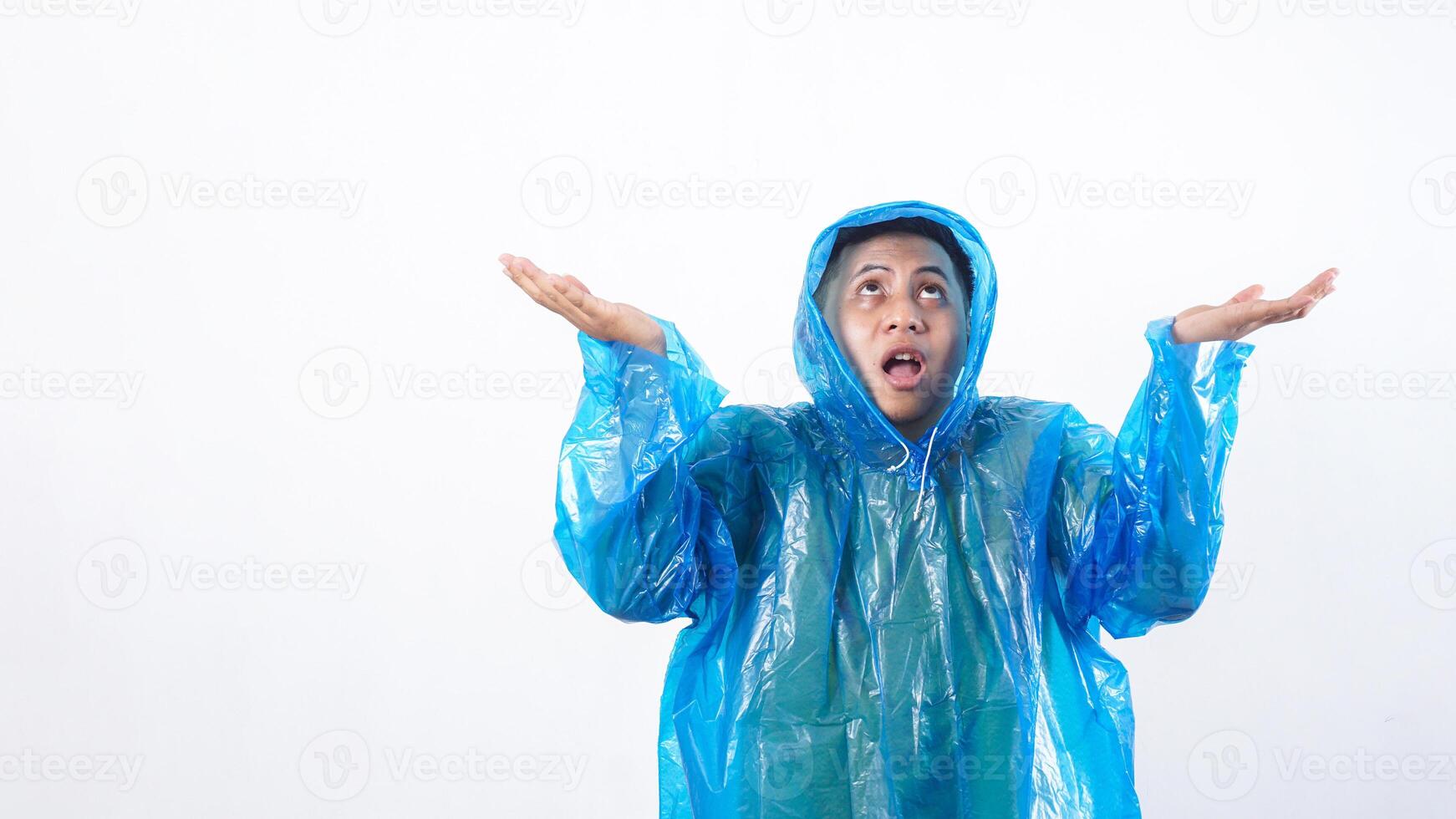 Portrait of Asian young man in blue raincoat expecting rain drops with worried expression isolated on white background photo