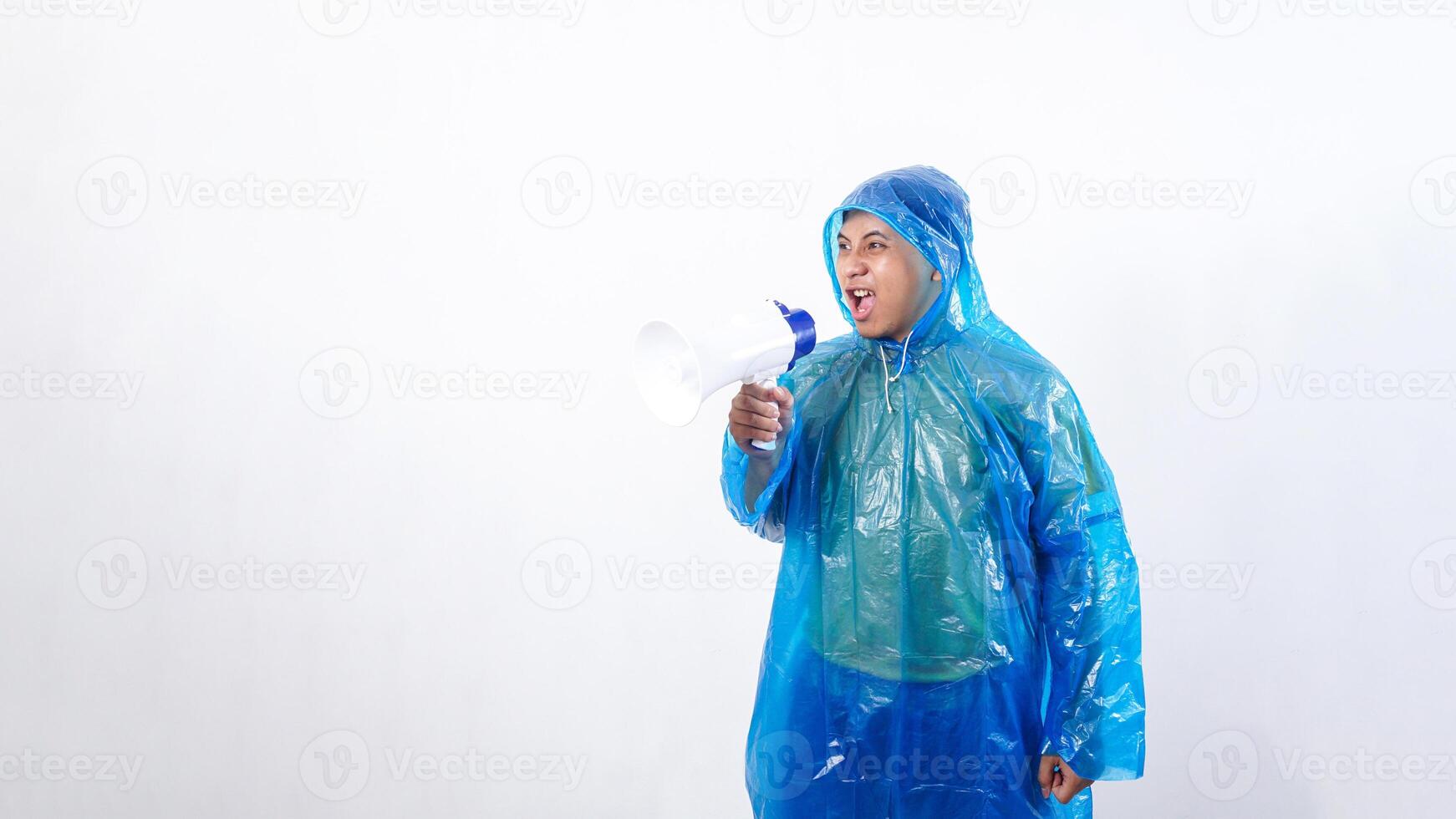 Angry Asian young man in blue raincoat shout using megaphone isolated on white background photo