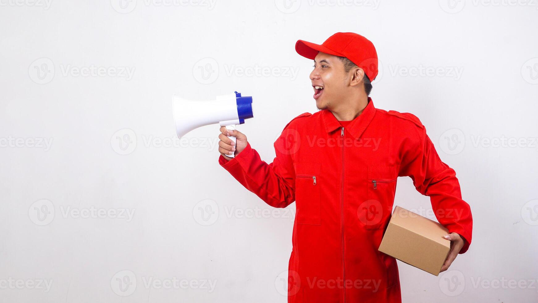 Portrait of Asian Delivery man in red uniform carrying a package box parcel while shout using megaphone isolated on white background photo
