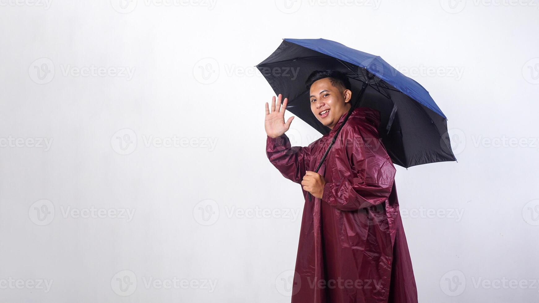 Happy Asian man in red raincoat and holds umbrella showing gesture to greeting people isolated on white background photo