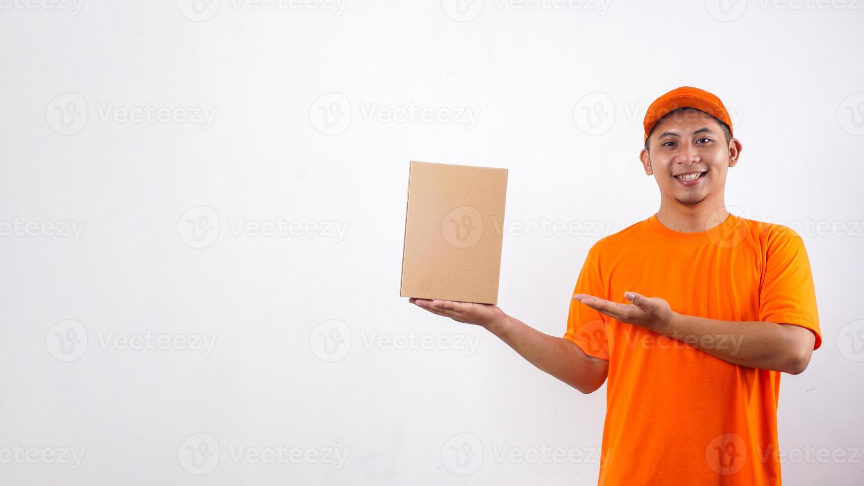 Asian deliveryman in orange t-shirt uniform poses as if he is presenting a package box parcel isolated on white background photo