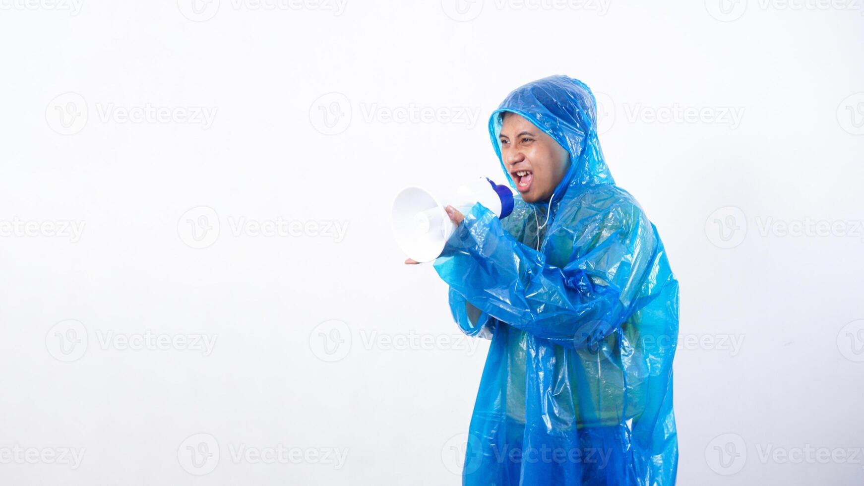 Angry Asian young man in blue raincoat shouting on megaphone isolated on white background photo