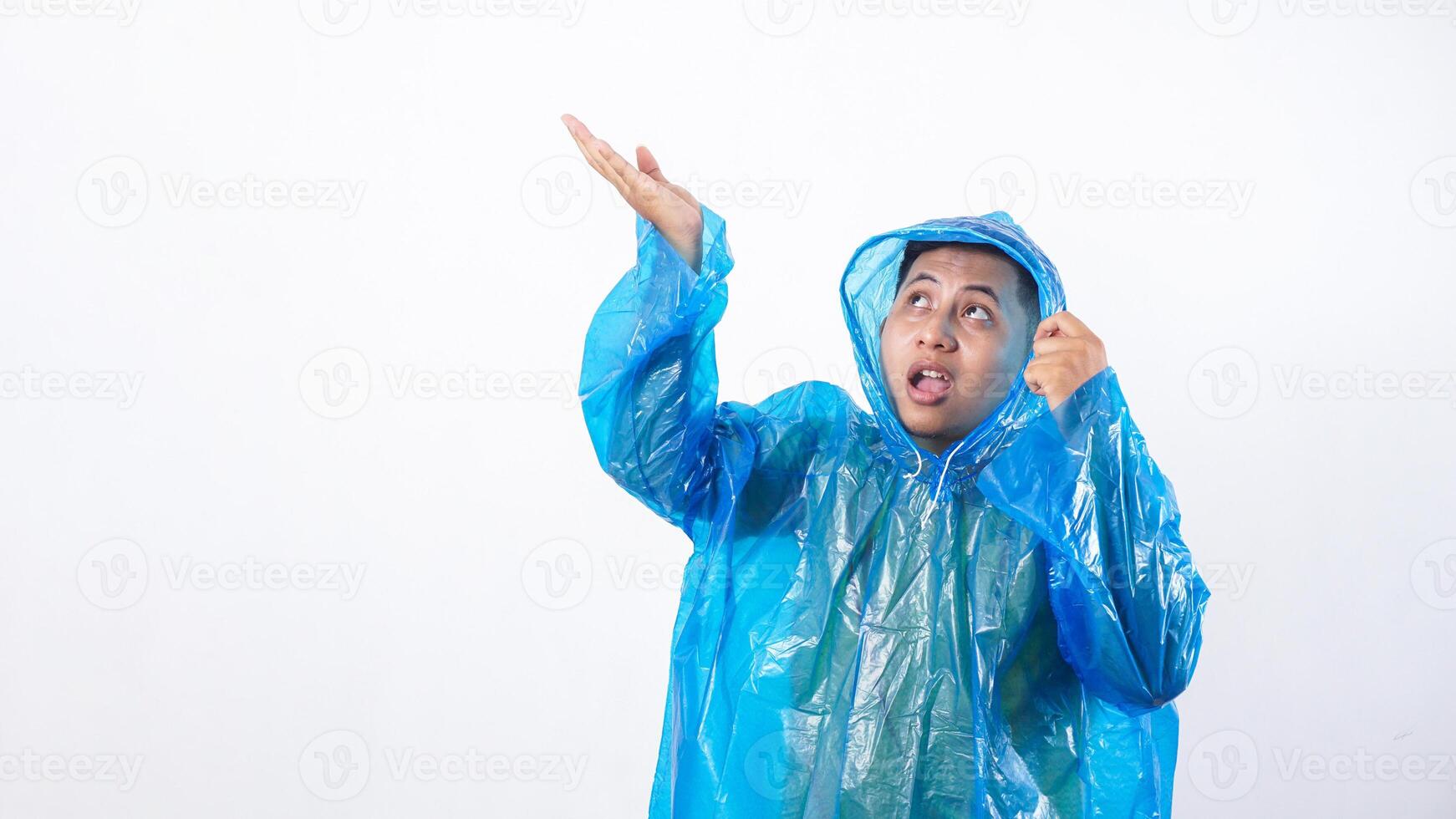 Asian young man in blue raincoat expecting rain drops with worried expression isolated on white background photo