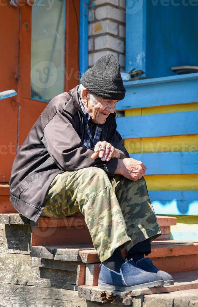 Smiling elderly Russian man with a cigarette, gazing into the distance with hope and peace, a rare moment of warmth in a hard rural life photo