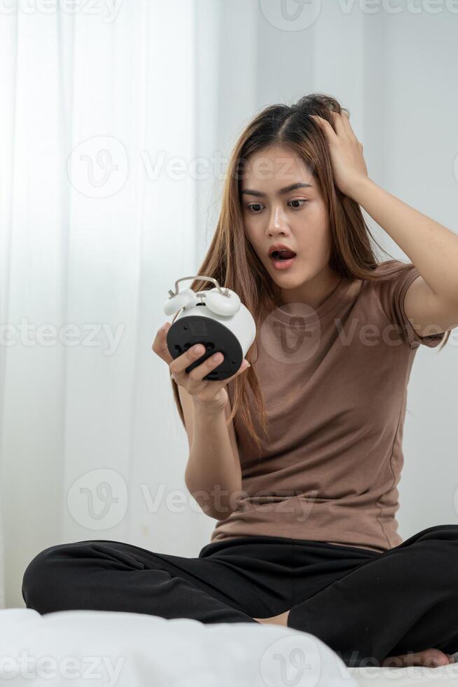 Shocked Asia young woman looking at clock alarm, lady is late appointment or work or class study, overslept, difficulty get up in mornings, time worried, not on time, sleepy, over due, photo