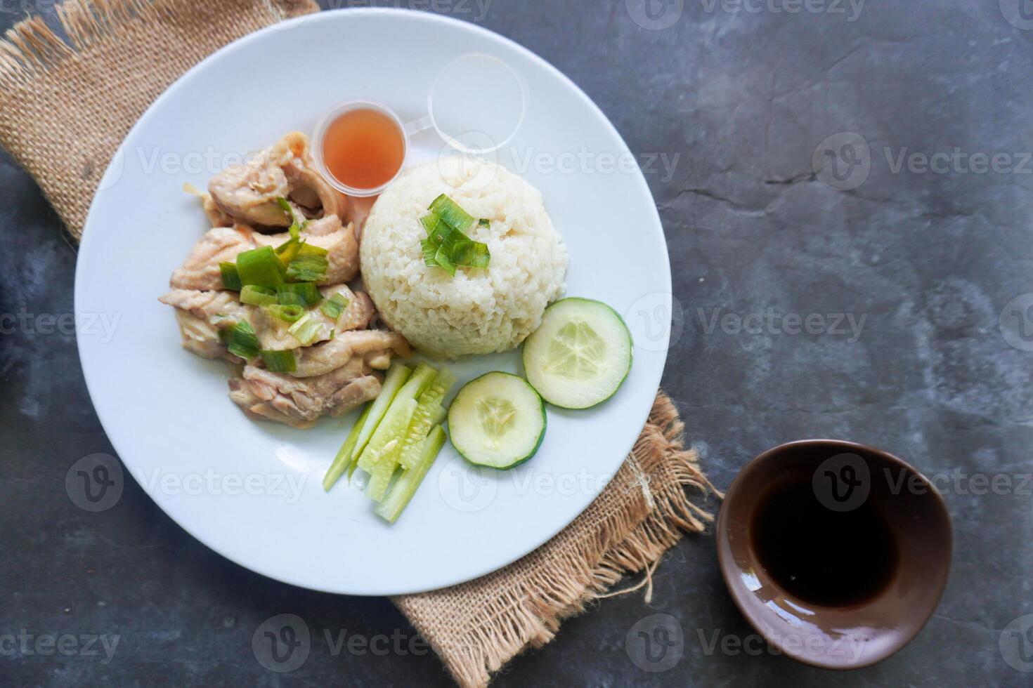 Hainanese chicken rice or rice steamed with chicken soup served with cucumber slice, broth, and sauce photo