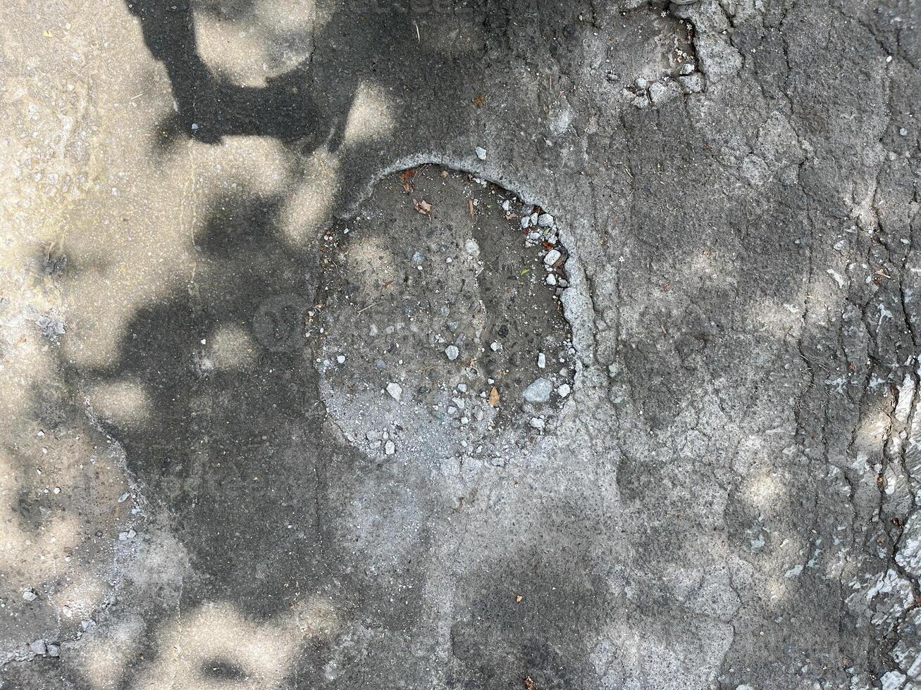 A grey concrete surface with a hole in the middle. The hole is surrounded by gravel and dir photo