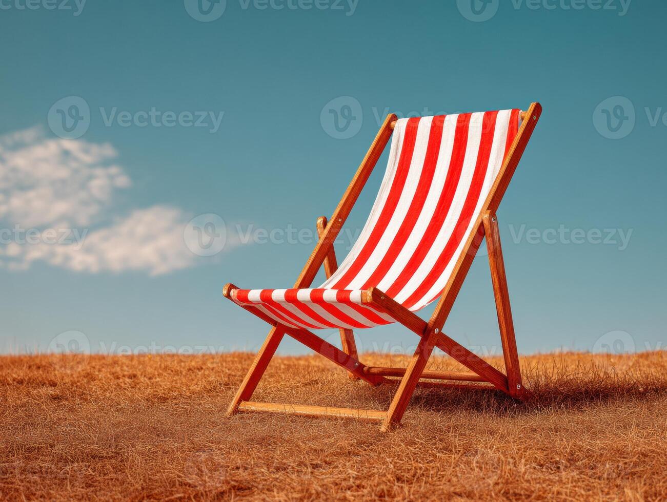 A red and white striped beach chair sitting on a dry field photo