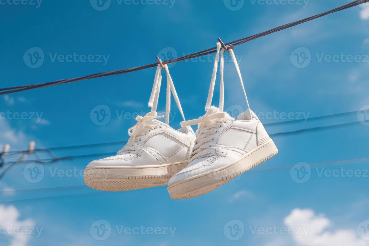 White sneakers hanging on a wire with blue sky background photo