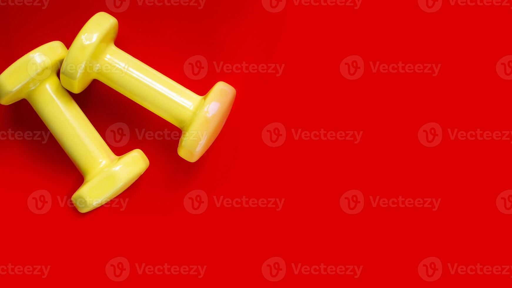 two yellow dumbbells on red background.wide banner photo