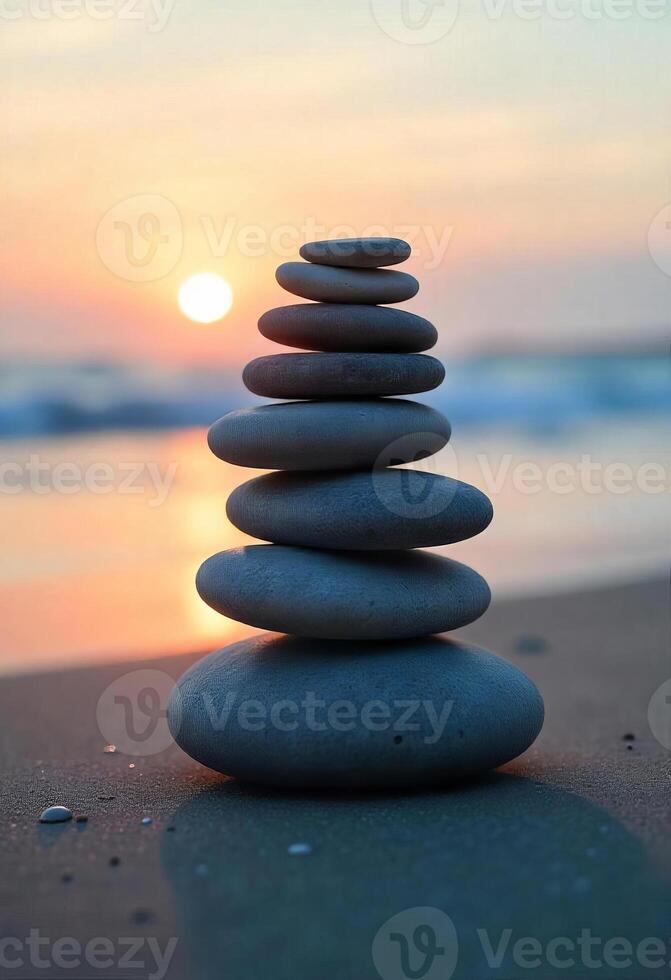 Stack of seven gray stones on the sand, with the sea in the background and the sun setting in the horizon photo