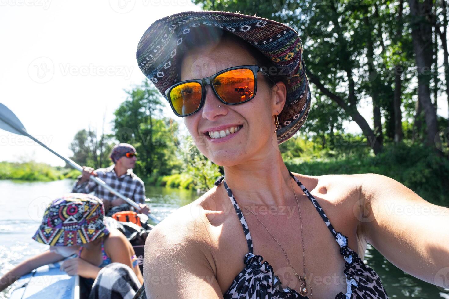A woman in a hat and sunglasses is taking a selfie in a canoe photo