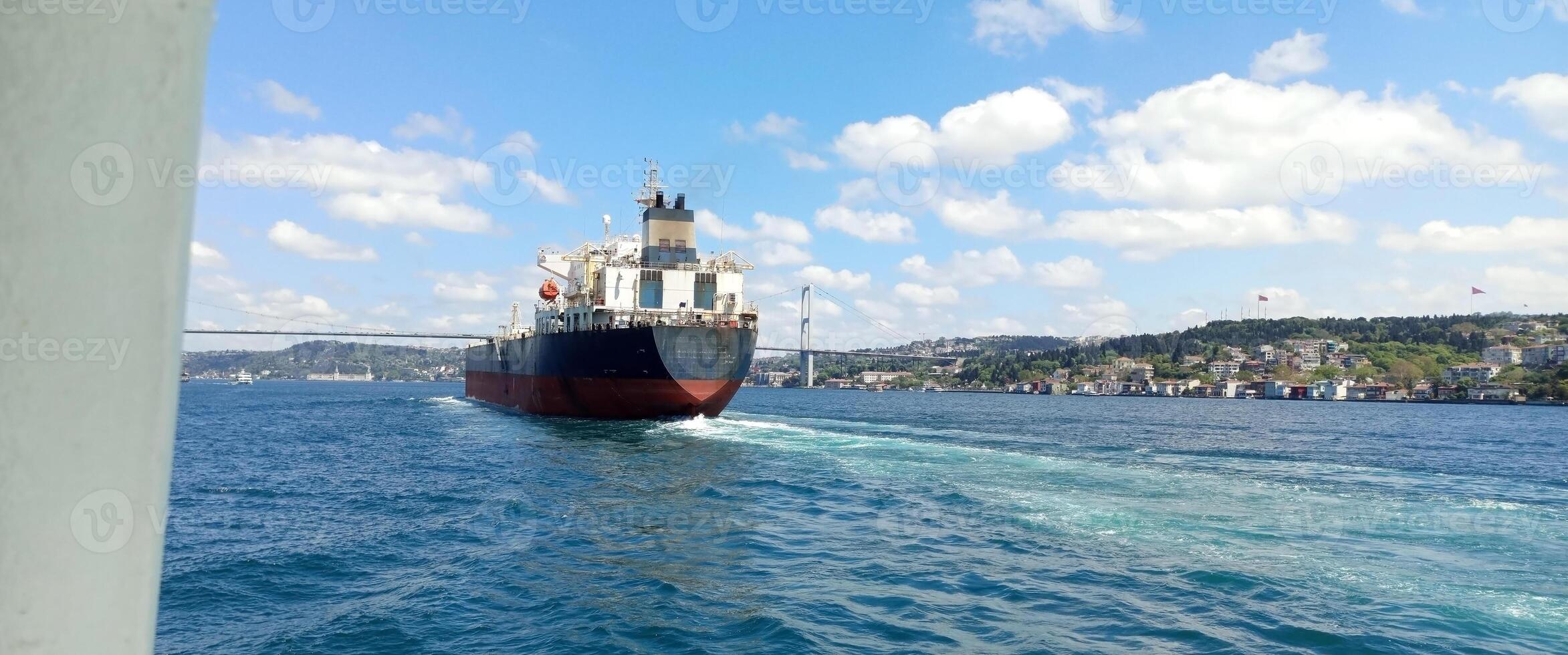 Large cargo ship navigates through the Bosphorus Strait near Istanbul under a bright blue sky with scattered clouds photo