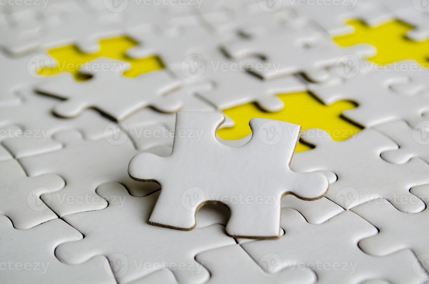 Close up of white jigsaw puzzle pieces placed on a bright yellow background with customizable space on jigsaw for text or ideas. photo