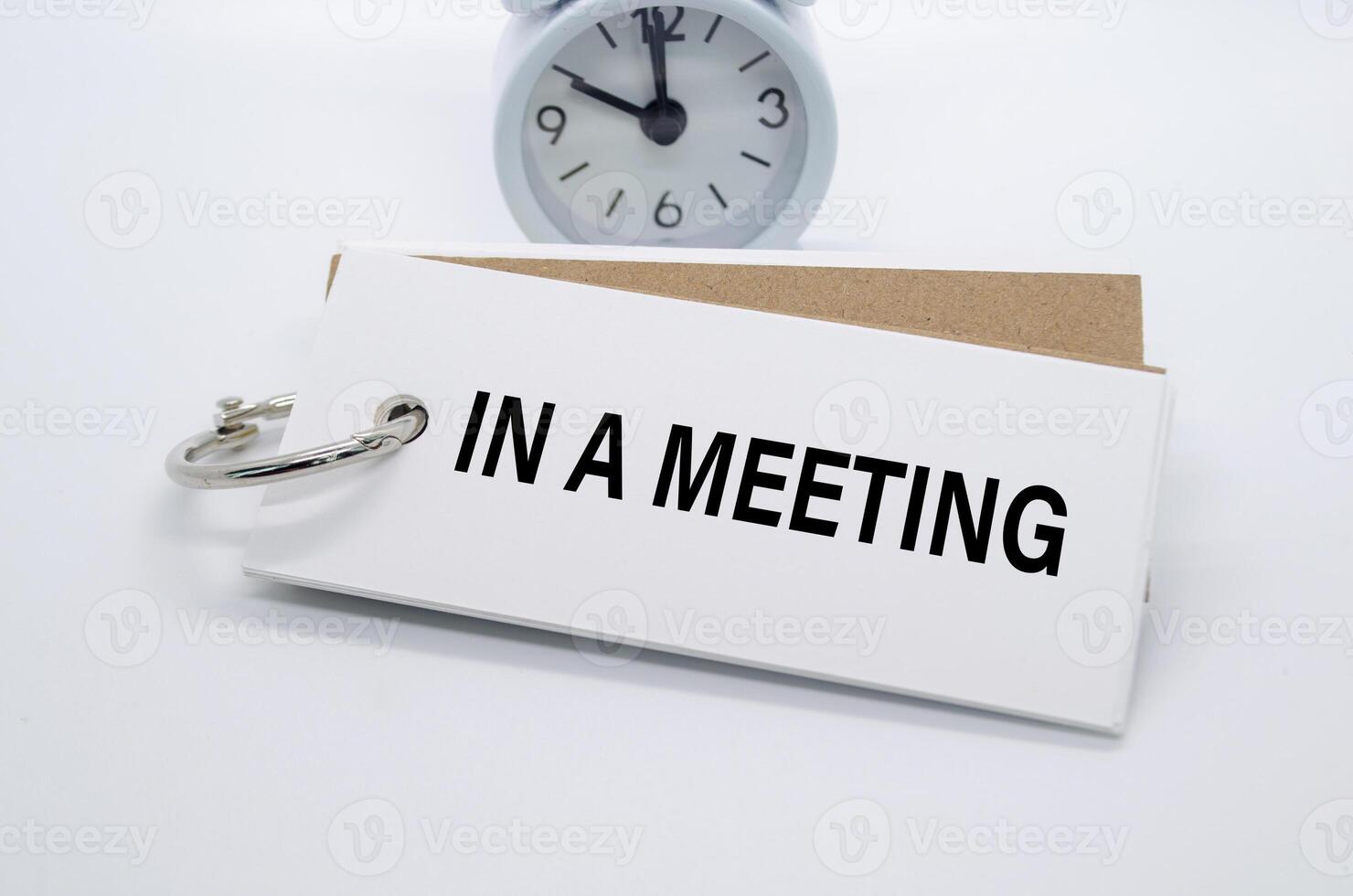 In A Meeting text on white notepad with alarm clock on white background. Away from office concept. photo