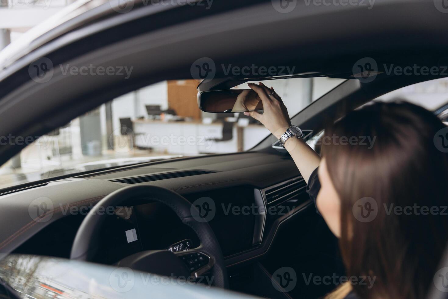 Customer Adjusting Rearview Mirror in New Car at Dealership photo