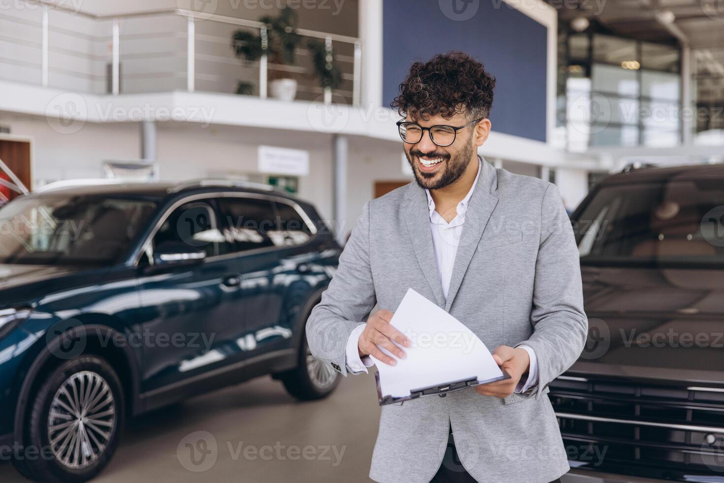 Car salesman holding documents and smiling in a car dealership photo