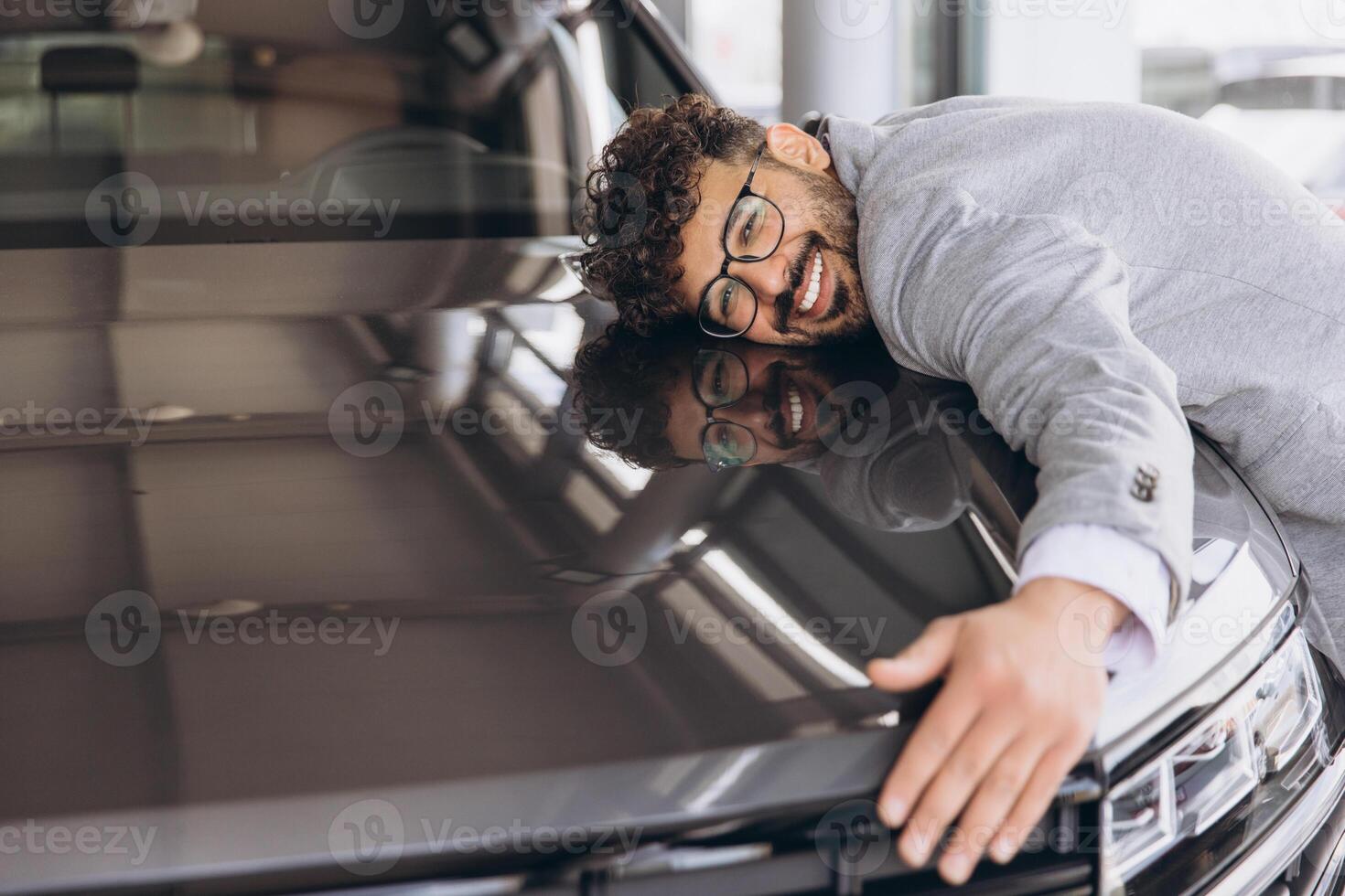 Smiling man hugging a car in a modern showroom photo