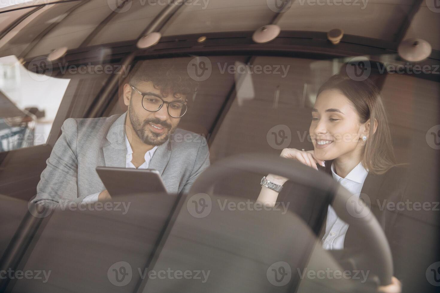 Car salesman showing tablet to customer sitting in new car photo