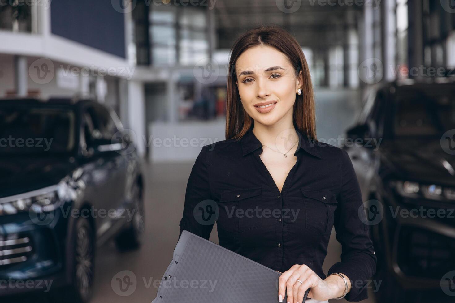 Saleswoman holding clipboard and posing in car dealership photo