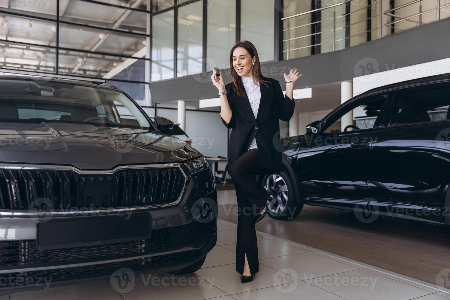 Businesswoman showing car key celebrating new purchase in car dealership photo