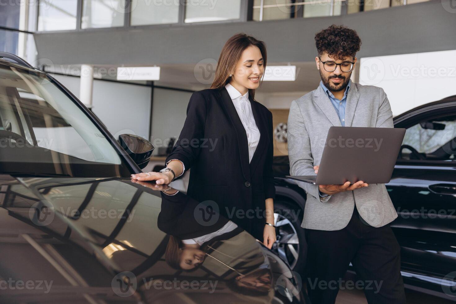 Car salesman showing features on laptop to customer buying new car photo