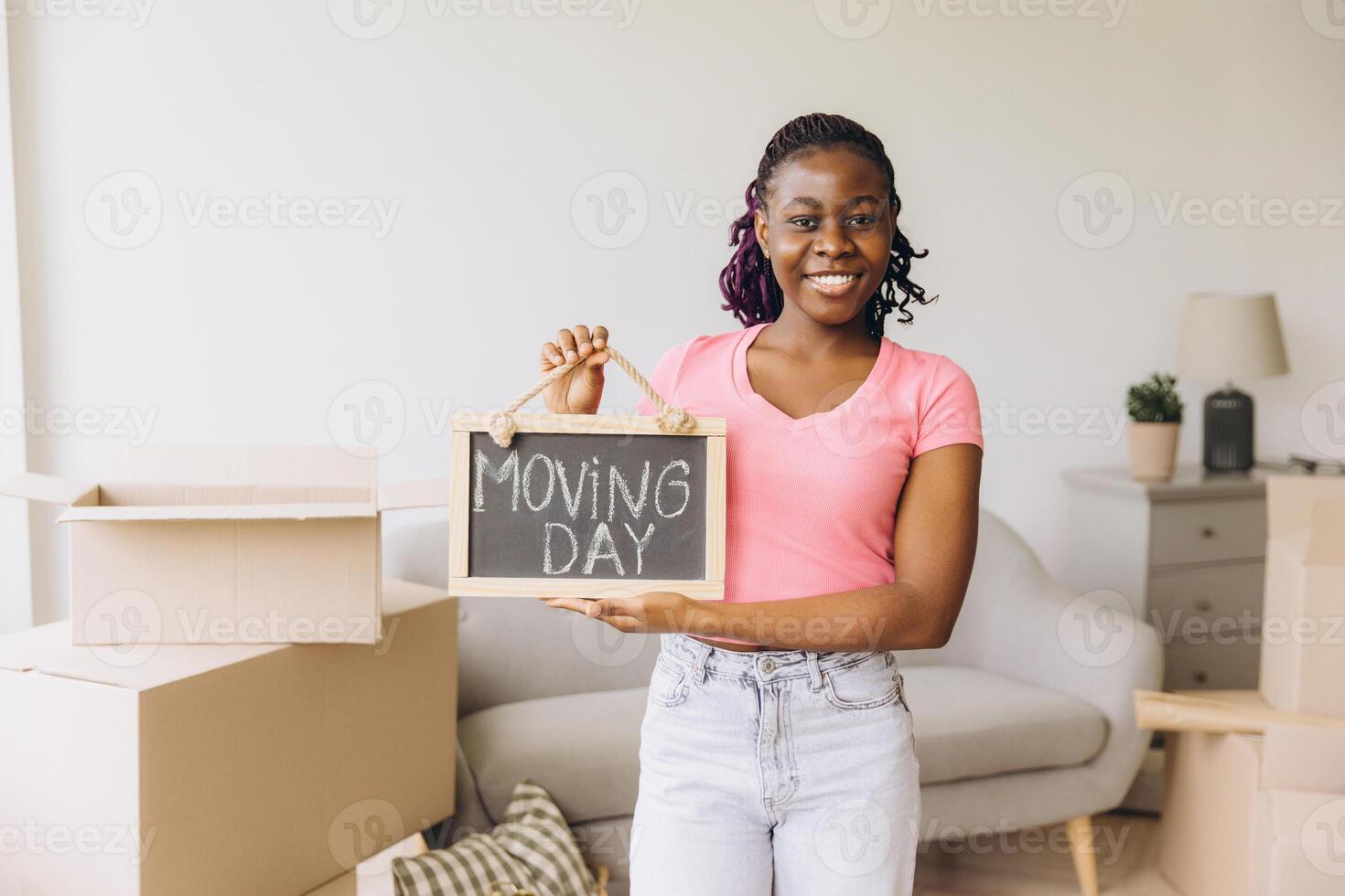 Happy African American woman holding moving day sign in new apartment photo