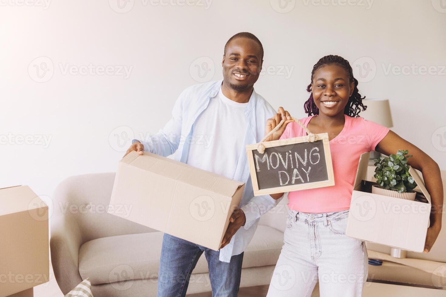 Happy african american couple moving to new house holding boxes and moving day sign photo