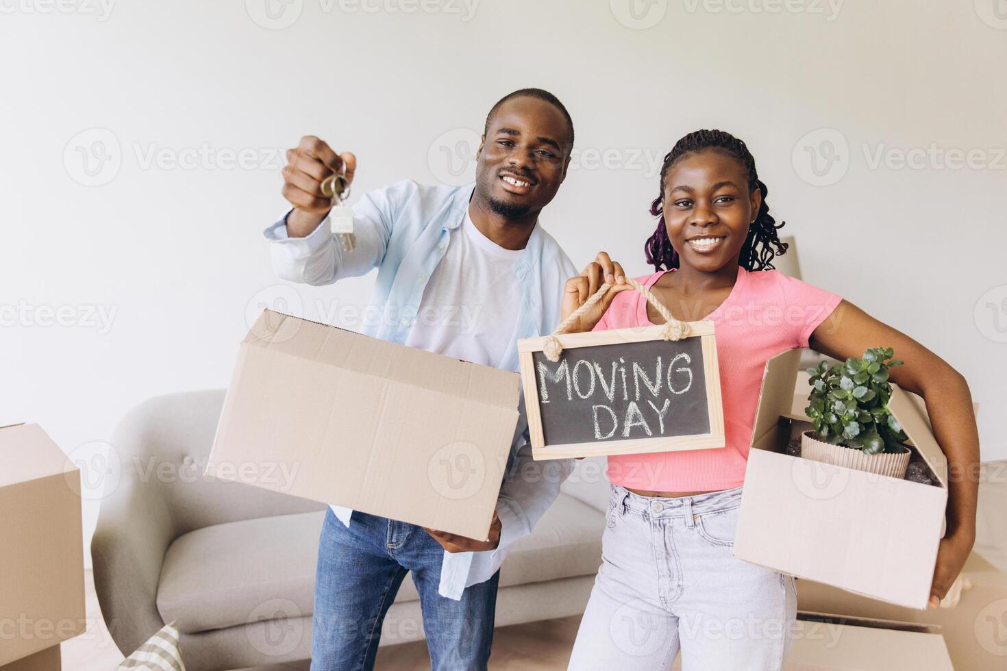 Happy African American Couple Holding Keys and Moving Day Sign in New Home photo
