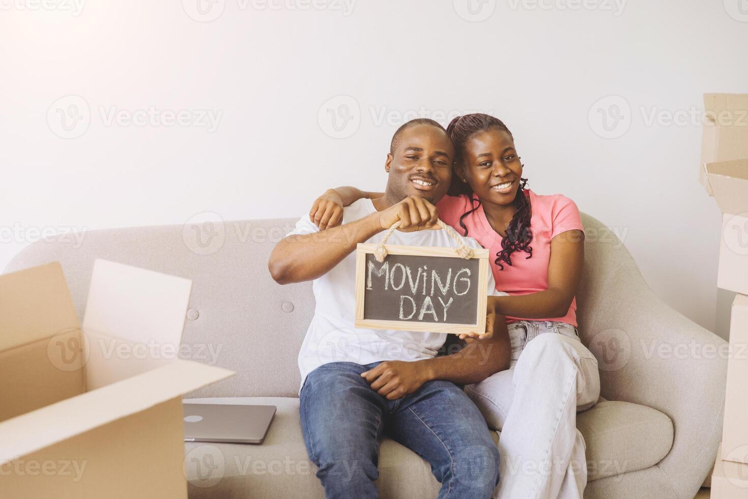 Happy African American Couple Showing Moving Day Sign While Sitting on Sofa photo