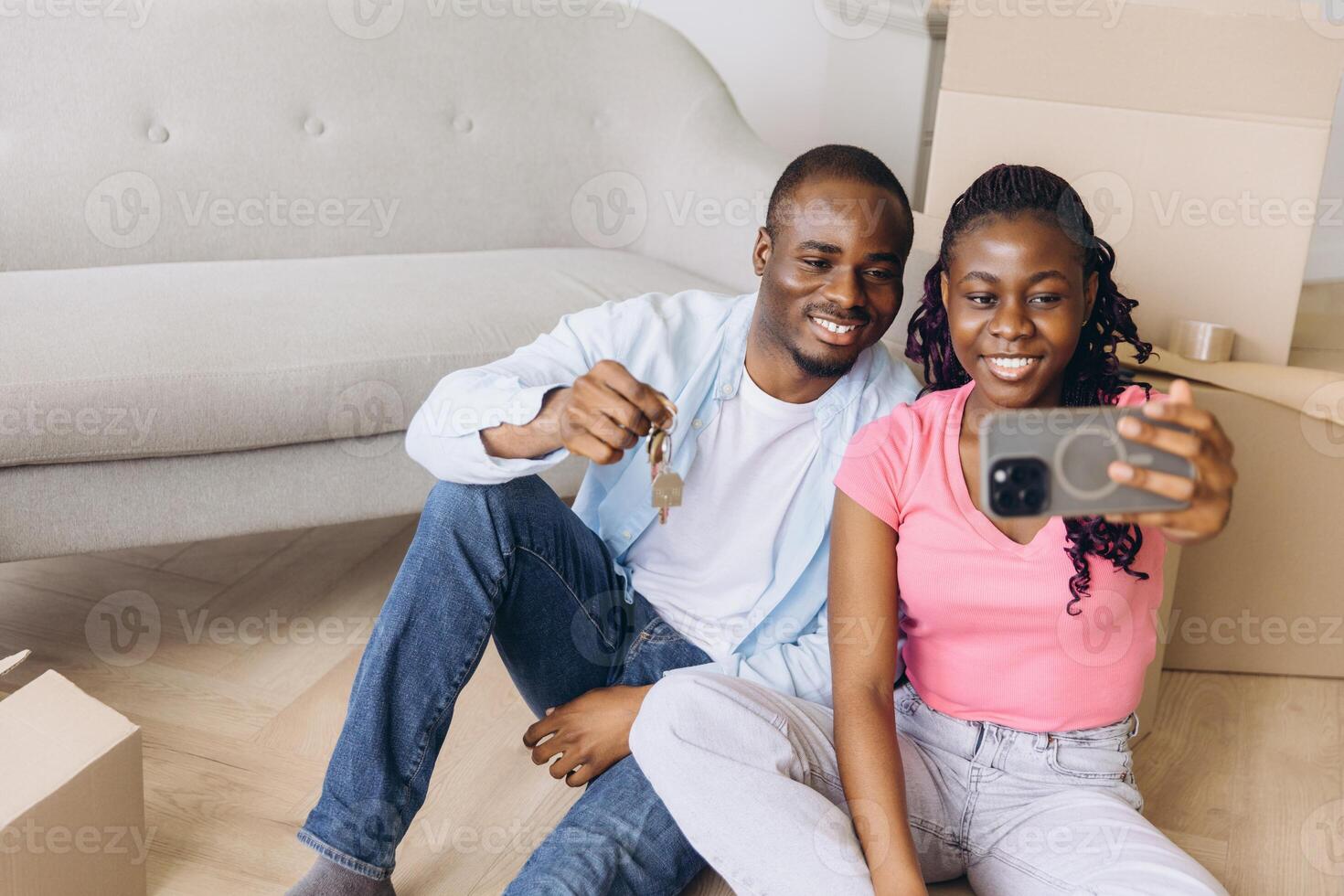 Happy african american couple taking a selfie and showing house keys in their new apartment photo