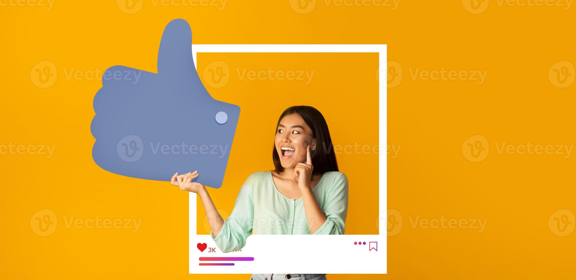 A young woman joyfully poses with a large thumbs-up symbol against a vibrant orange background, expressing enthusiasm for her online content. This moment highlights her connection with followers. photo