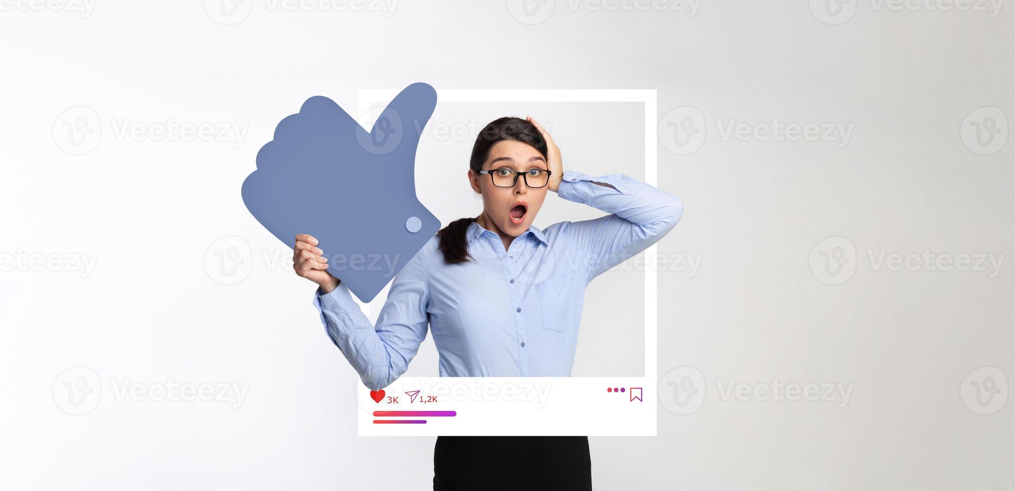 A surprised influencer stands in a studio, holding a large like symbol and expressing excitement. The backdrop features a collage of social media elements, enhancing the theme of digital content. photo