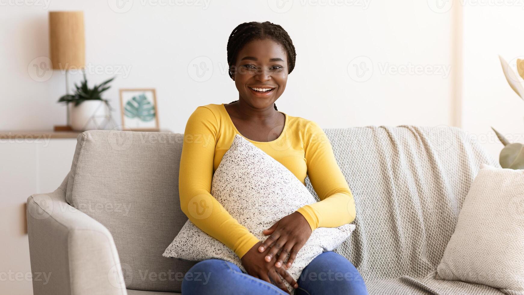 Day At Home. Smiling Black Woman Sitting On Comfortable Couch With Pillow, Attractive African American Lady Posing At Camera In Cozy Living Room Interior, Enjoying Domestic Leisure, Free Space photo