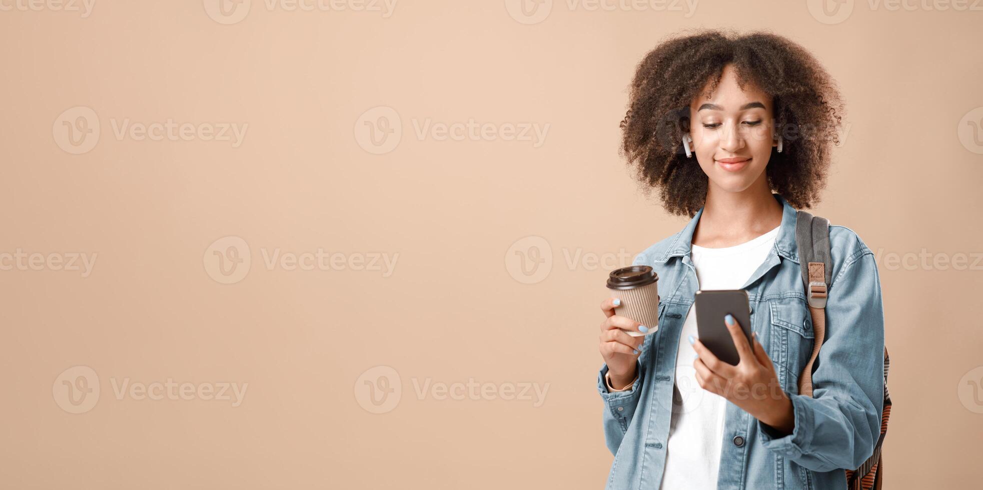 Watch movie, read blog, get message and active lifestyle. Friendly calm african american woman looking on smartphone holds cup of takeaway coffee isolated on light background, copy space, studio shot photo