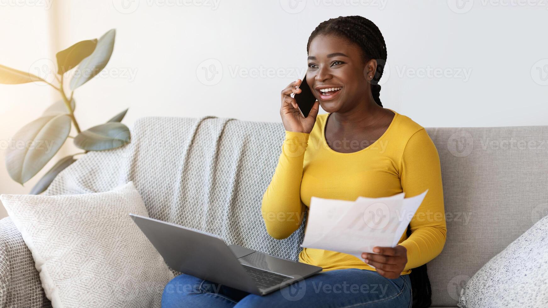 Work From Home. Smiling Black Freelancer Lady Talking On Cellphone While Working With Papers And Laptop On Couch In Living Room, African Lady Enjoying Remote Job And Mobile Communication, Copy Space photo