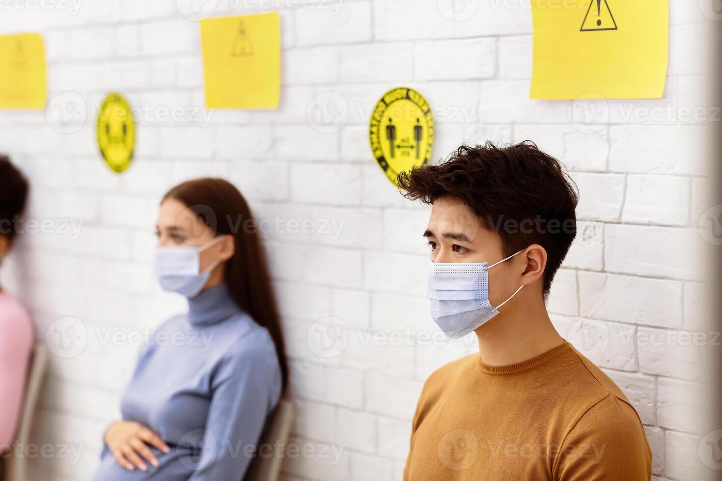 Covid-19 Vaccination. Chinese Man In Medical Mask Waiting To Receive Coronavirus Vaccine Injection Sitting In Queue In Hospital. Covid 19 Population Immunization Campaign, Corona Virus Prevention photo