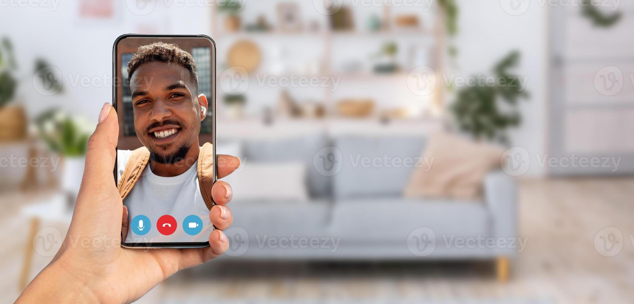 A person is having a cheerful chat on a smartphone while seated in a cozy living room. The background features a comfortable sofa and houseplants, creating a warm atmosphere. photo