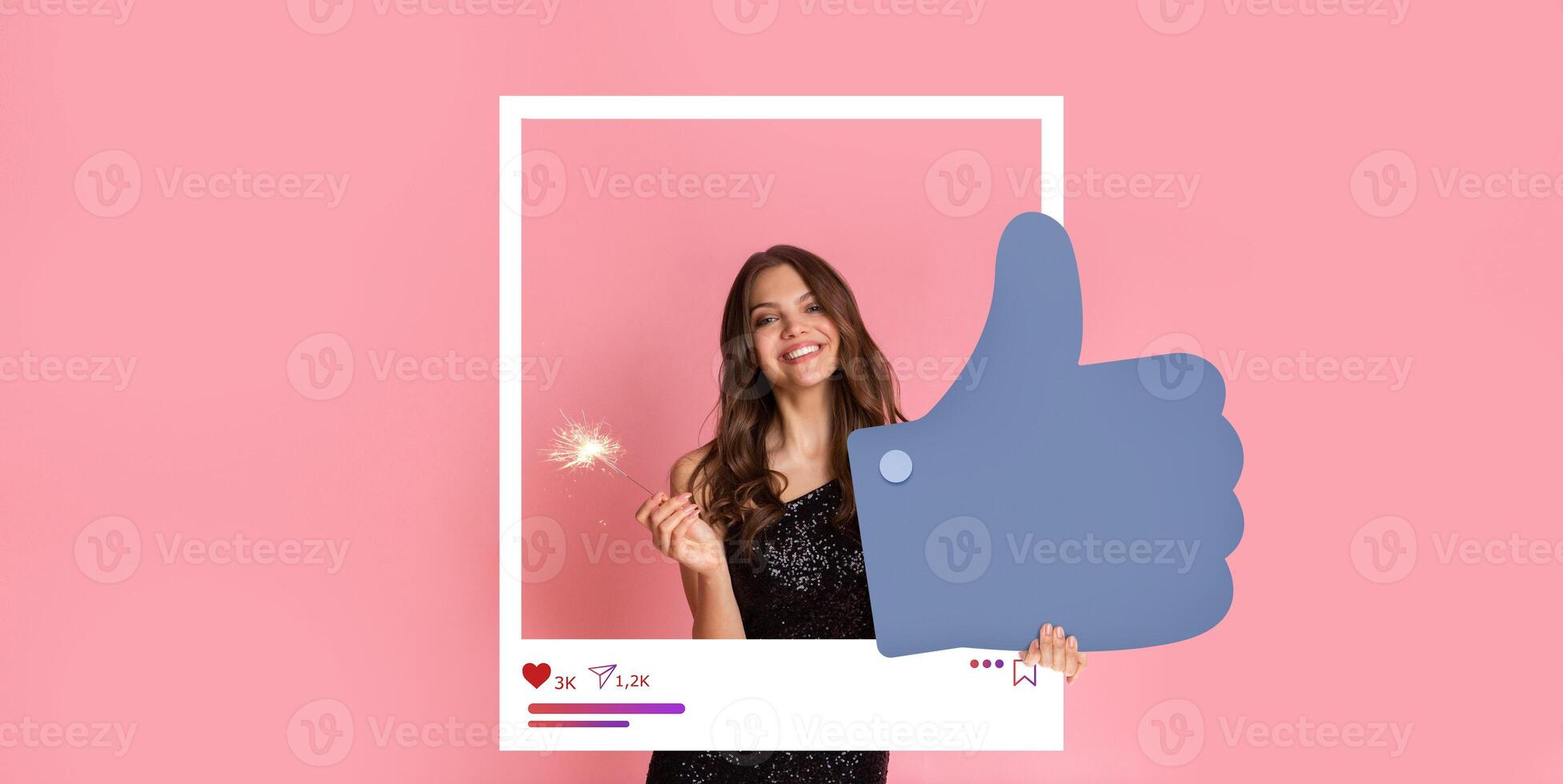 A young woman with long hair smiles and poses with a large thumbs up hand. She holds a sparkler, dressed in a sparkling outfit, against a pink background, embodying a fun social media moment. photo
