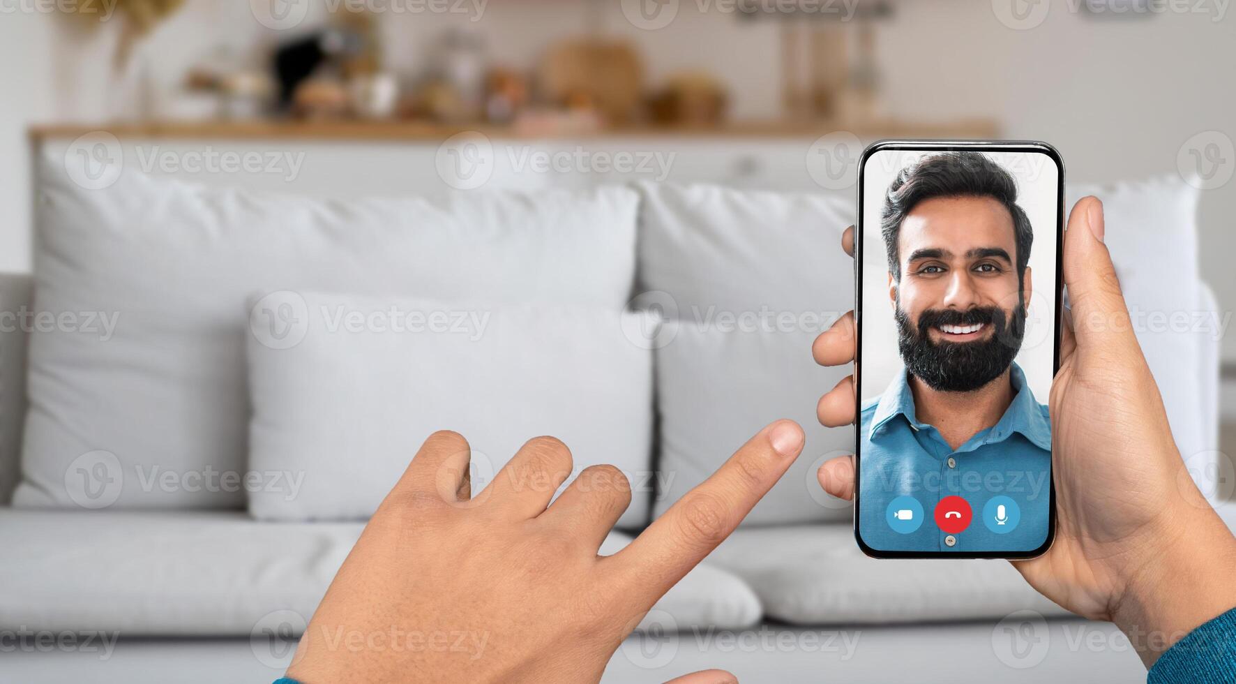 A person is using a smartphone to have an online call. The setting is a cozy home with a light-colored sofa in the background. The individual converses cheerfully. photo