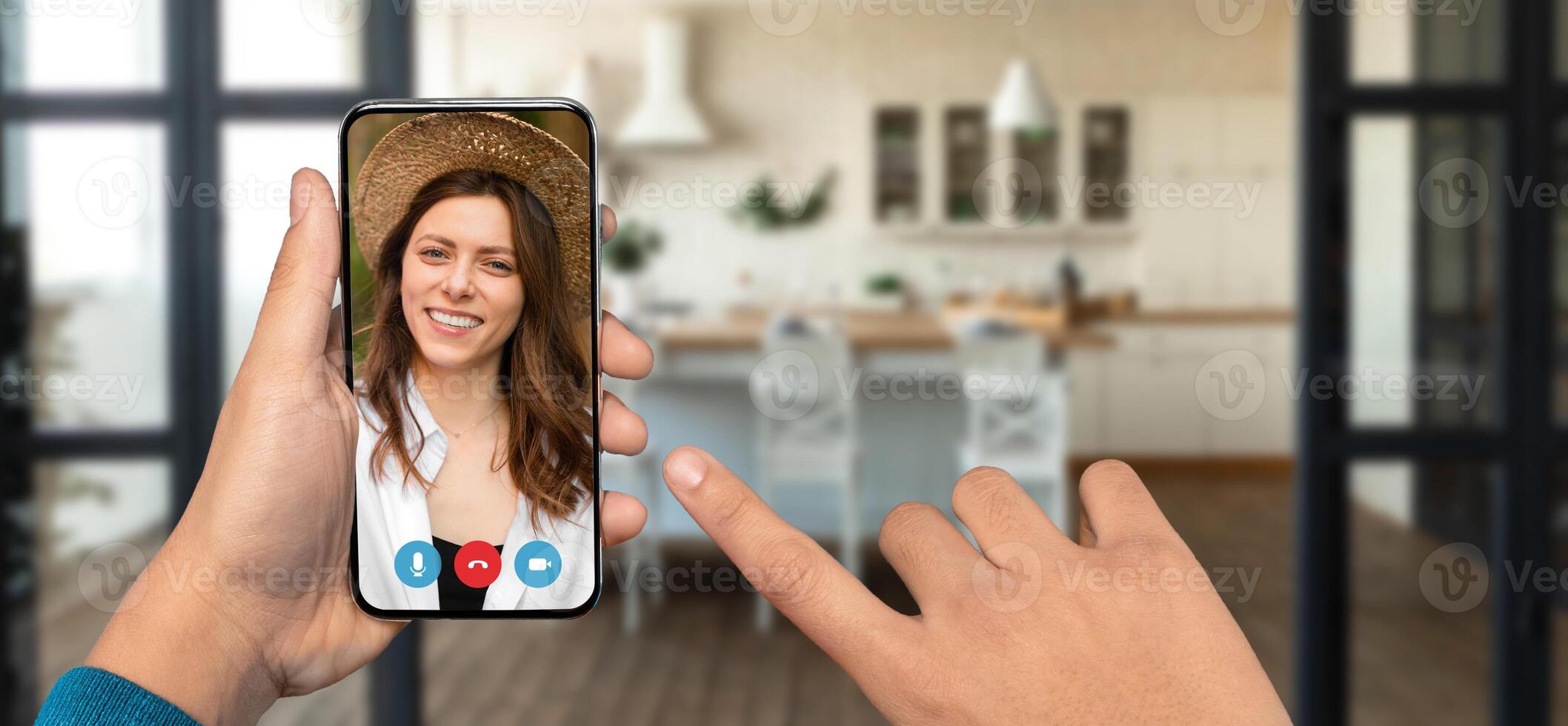 A person using a smartphone for a chat in a home setting, showcasing a bright kitchen interior. The individual on screen smiles while communicating, reflecting a casual atmosphere. photo