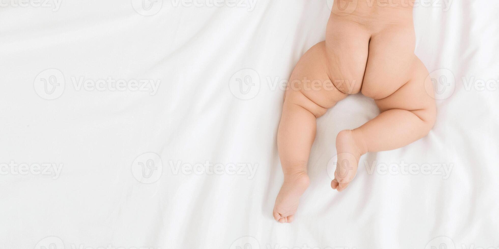 Adorable naked baby butt and legs on white bed. Dry and healthy body and skin, panorama with empty space, top view photo