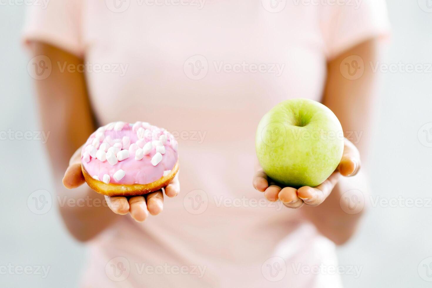 Choice of healthy or junk food. Closeup view of black woman choosing between donut and apple on light background. Millennial lady making decision about her snack, facing temptation photo