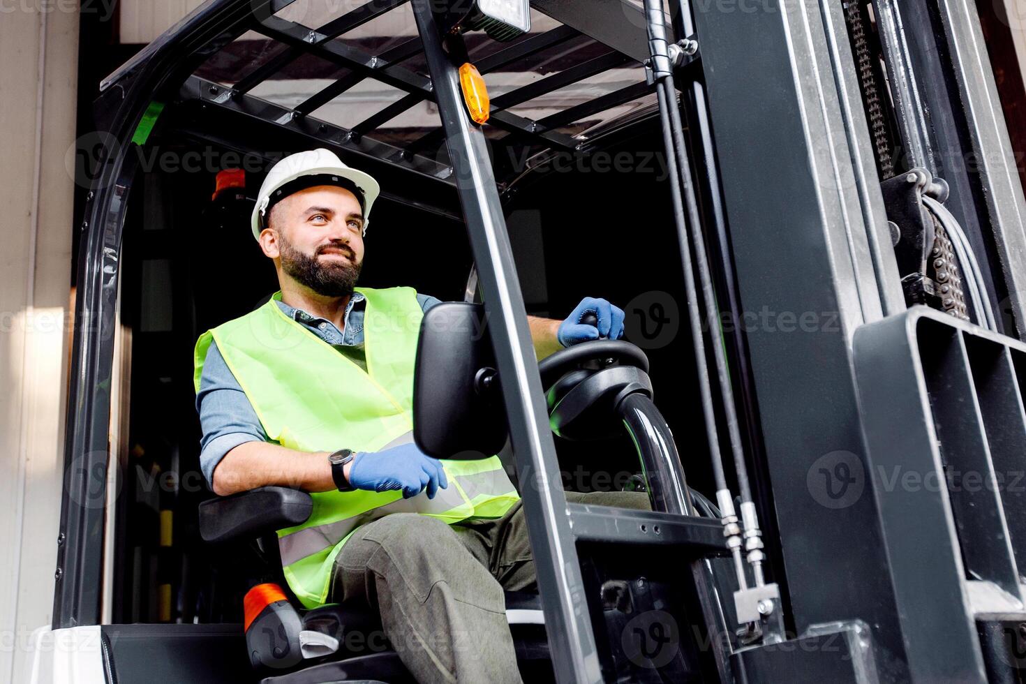 Work in warehouse, loading organic fruits for sale and production of juices. Smiling guy driver in helmet in forklift truck lifts up wooden container full of red ripe apples, on storage background photo