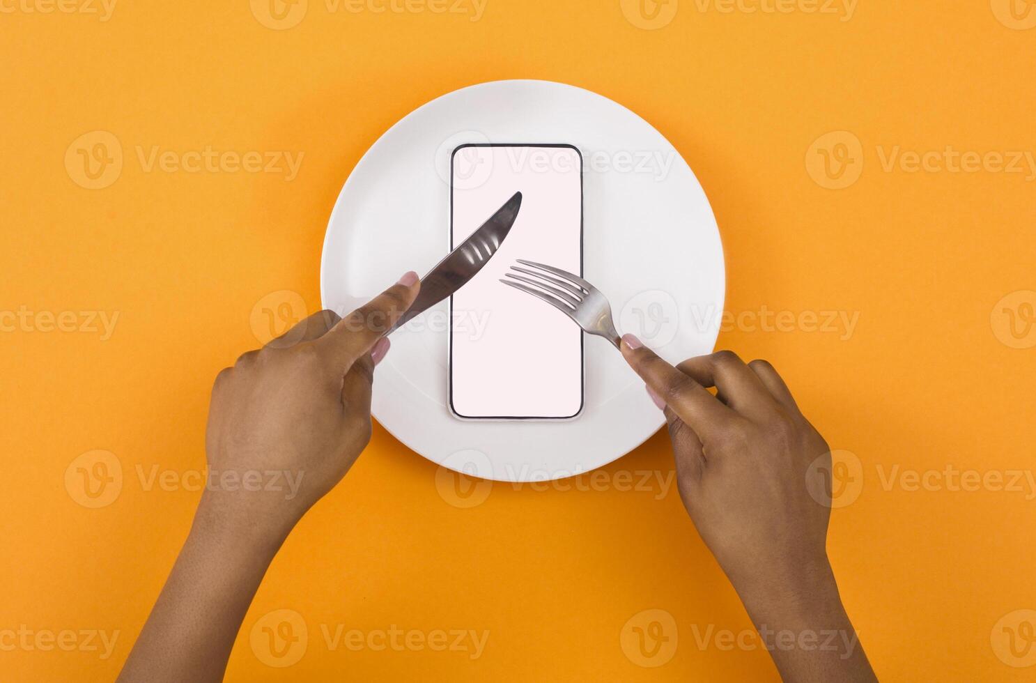 Absorption of information. African american woman eating blank smartphone with knife and fork, top view, mockup photo
