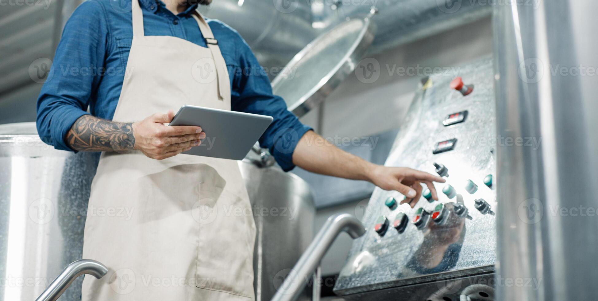 Male worker on beer factory, management and mobile app. Busy male employee or owner in apron with digital tablet controls equipment at brewery and push button, cropped, free space, panorama photo